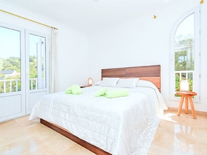 Ein Schlafzimmer mit einem großen Bett, einem hölzernen Kopfteil und Blick ins Grüne.