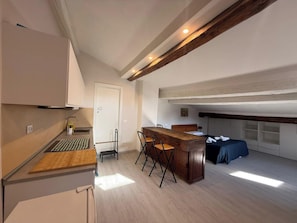 A compact kitchen with a wooden countertop, a dining area with a bar stool, and a bed with a dark blue bedspread. - Il Pittore by Interhome (Pisa)