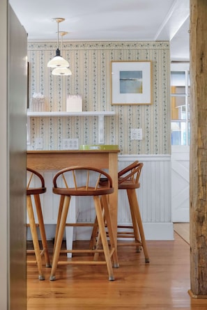 Eine Küche mit einer Holzhocker-Sitzgruppe, einer hängenden Pendelleuchte und einem gerahmten Bild an der Wand.