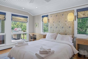A bedroom with a large bed, a desk, and a window with a view of greenery.