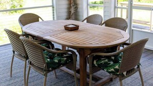 Uma mesa de madeira redonda com design de cadeira trançada, rodeada por seis cadeiras de vime com almofadas estampadas.