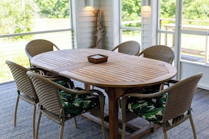 Ein runder Holztisch mit Flechtstuhl-Design, umgeben von sechs Korbstühlen mit gemusterten Sitzkissen.