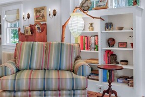 Un saló tranquil amb un sofà a ratlles, una prestatgeria plena de llibres i una làmpada decorativa.