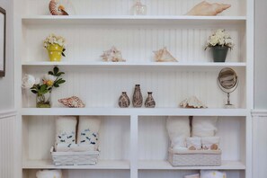 A white wooden shelf with decorative items including seashells, flowers, and vases.