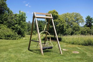 A wooden swing set in a grassy area with trees in the background.