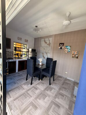 A dining area with a glass table and chairs, a ceiling fan, and a kitchen in the background. - (Paz) A place to stay and enjoy with the family. (Sosúa)