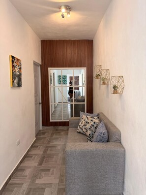 A hallway with a grey sofa, wooden paneling, a ceiling fan, and a door leading to a room. - (Paz) A place to stay and enjoy with the family. (Sosúa)