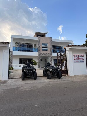 A multi-story building with a rental sign, two ATVs parked in front, and a clear sky. - (Paz) A place to stay and enjoy with the family. (Sosúa)