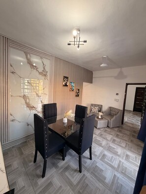 Un coin repas avec une table en verre et des chaises noires, un mur avec des stores verticaux et un ventilateur de plafond.