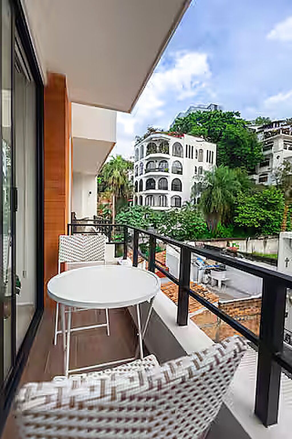 Un balcon avec une table ronde et deux chaises, donnant sur un immeuble doté de nombreux balcons et agrémenté de verdure.