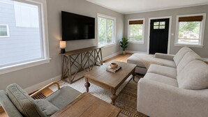 A living room with a flat-screen TV mounted on the wall, a wooden coffee table, a beige sofa, and a patterned rug. - Spacious Coastal-Style Home in Ravenna — Steps to UW, U-Village Mall, and more! (Seattle)