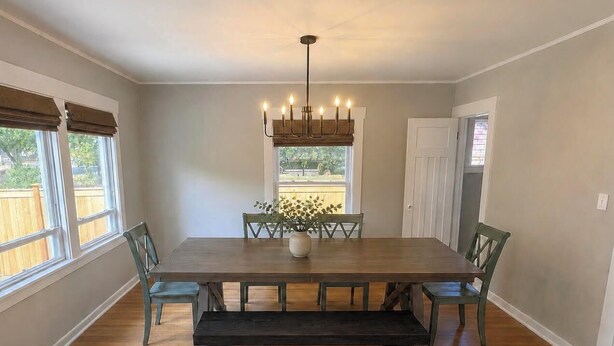 A dining room with a large wooden table, six chairs, a bench, a chandelier, and a window with a view of greenery. - Spacious Coastal-Style Home in Ravenna — Steps to UW, U-Village Mall, and more! (Seattle)