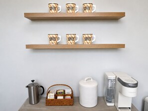 Two wooden shelves with coffee mugs, a coffee maker, a kettle, a water dispenser, and a basket of coffee pods. - Spacious Coastal-Style Home in Bryant — Steps to UW, U-Village Mall, and more! (Seattle)