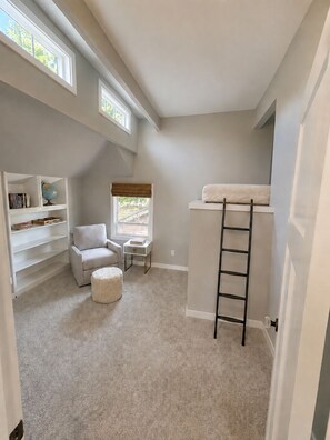 Quarto compacto com beliche, um pequeno espaço de estar e uma estante.