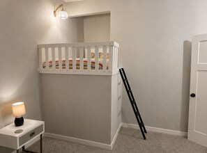 Ein Kinderstockbett mit einer Leiter, ein Nachttisch mit Lampe und eine Tür.