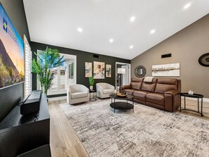 A modern living room with a brown leather sofa, two white armchairs, a coffee table, and a large potted plant.