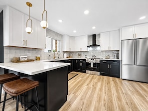 A modern kitchen with white cabinetry, a central island with stools, stainless steel appliances, and pendant lighting.