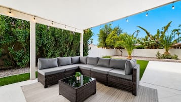 Un espace extérieur aménagé, abrité et doté d’un canapé d’angle et d’une table basse avec un plateau en verre.