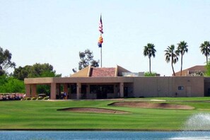 A building with a flat roof, a flagpole with flags, and a well-maintained lawn with a water feature.