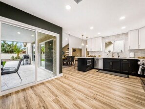 A modern kitchen with a large island, black cabinetry, and a sliding glass door leading to an outdoor patio.