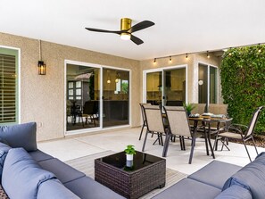 Un patio al aire libre con un ventilador de techo, una mesa de comedor con sillas y una zona de estar con sofás.