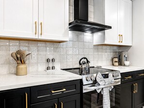 Una cocina moderna con gabinetes blancos y negros, una estufa de acero inoxidable y una campana extractora negra sobre la cocina.