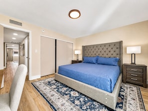 A bedroom with a large bed, two bedside tables with lamps, a chair, a wardrobe, and a patterned rug.