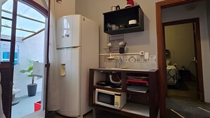 Cocina compacta con refrigerador, microondas y un estante con utensilios de cocina.