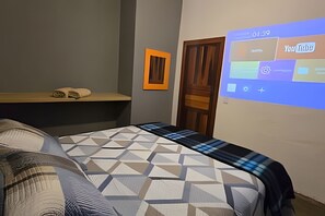 Un dormitorio con cama, mesita de noche, proyector montado en la pared y una puerta.
