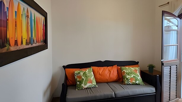 Una habitación con un sofá gris, dos almohadas naranjas y una obra de arte colorida enmarcada en la pared.