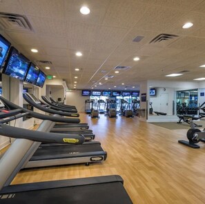 Ein Fitnessstudio mit Laufbändern, Trainingsgeräten und mehreren Bildschirmen, die Trainingsvideos zeigen.