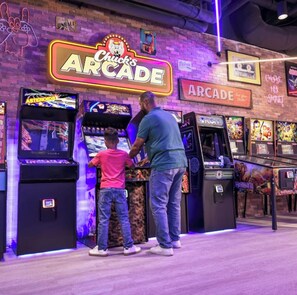 A man and a child playing arcade games at Chuck's Arcade. - Spacious 2 Bedroom Condo Family Retreat Minutes from Disney and Universal (Kissimmee)