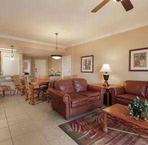 A living room with a brown leather sofa, a wooden coffee table, and a dining area with chairs and a table. - Spacious 2 Bedroom Condo Family Retreat Minutes from Disney and Universal (Kissimmee)