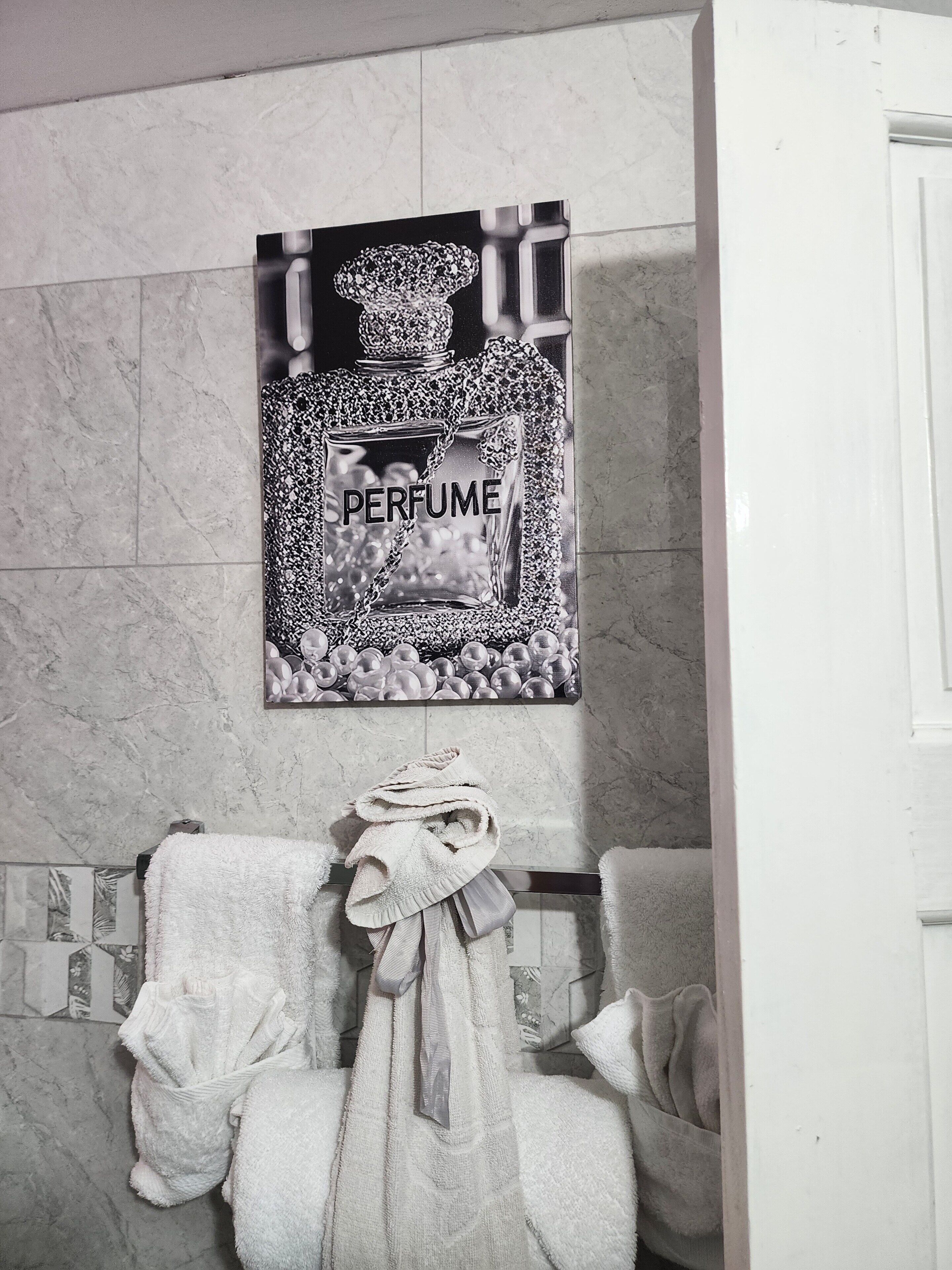 A bathroom with a marble wall, a framed perfume bottle artwork, and two towels on a rack.