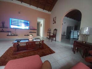 Sala de estar com televisão exibindo dados de sentimento do consumidor, uma mesa de centro de madeira, um sofá vermelho e uma área de jantar com luminária.