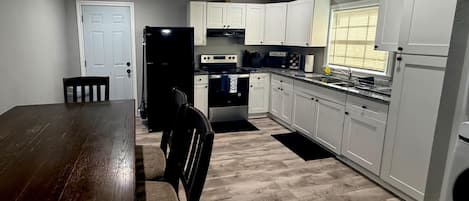 A kitchen with white cabinets, a dark wooden table, and a window with blinds.