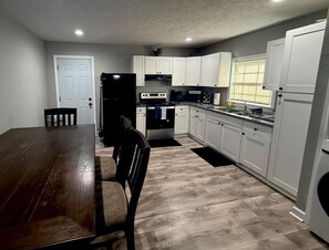 A kitchen with white cabinets, a dark wooden table, and a window with blinds. - 2-bedroom apartment in peaceful Houston with AC for relaxing stays (Houston)