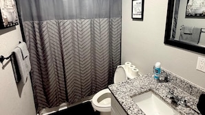 Une salle de bain avec un rideau de douche, des toilettes, un lavabo et un tableau encadré au mur.