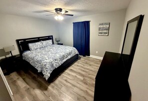 A bedroom with a bed, a nightstand, a ceiling fan, a wall-mounted mirror, and a motivational quote on the wall. - 2-bedroom apartment in peaceful Houston with AC for relaxing stays (Houston)