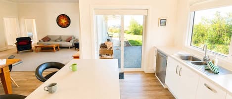 Uma cozinha moderna com uma ilha grande, uma área de jantar com sofá e cadeiras, e vista para o exterior através de uma porta deslizante.