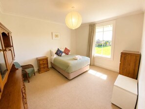A bedroom with a bed, a nightstand, a dresser, a window with curtains, and a hanging light fixture. - Otere River View Villa - Golden Bay (Onekaka)