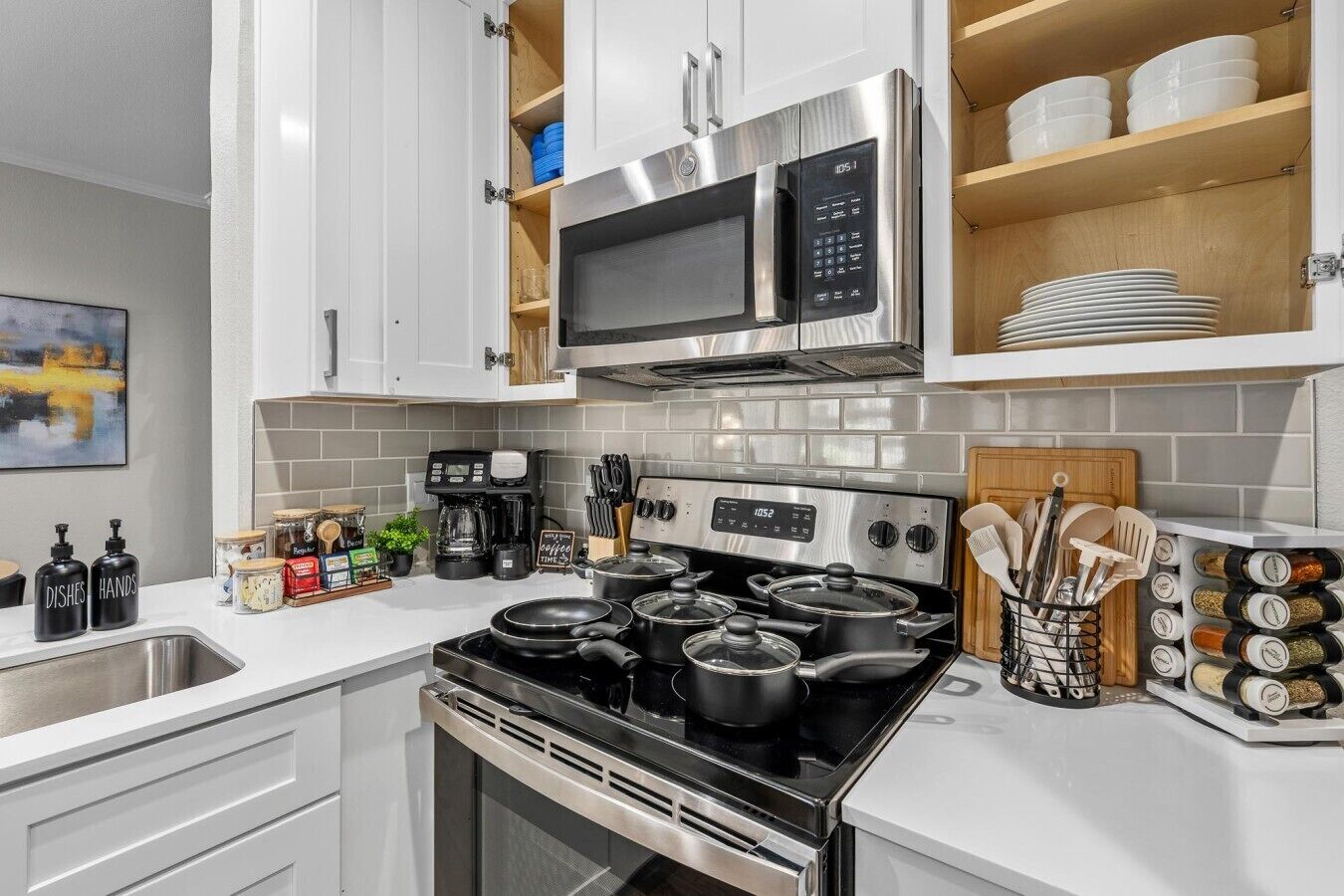 A modern kitchen with white cabinetry, a stainless steel stove, a microwave, and various kitchen utensils.