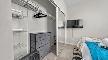 A bedroom with a bed, a dresser, a closet with shelves, a TV, and a fan.