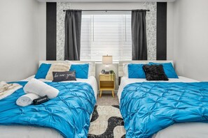 Een hotelkamer met twee bedden, een nachtkastje, een lamp en een raam met jaloezieën.