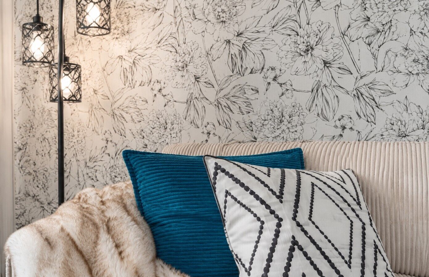 Ein Zimmer mit blumigem Wandpapier, einem Fellüberwurf und einem gemusterten Kissen auf einem Sofa.