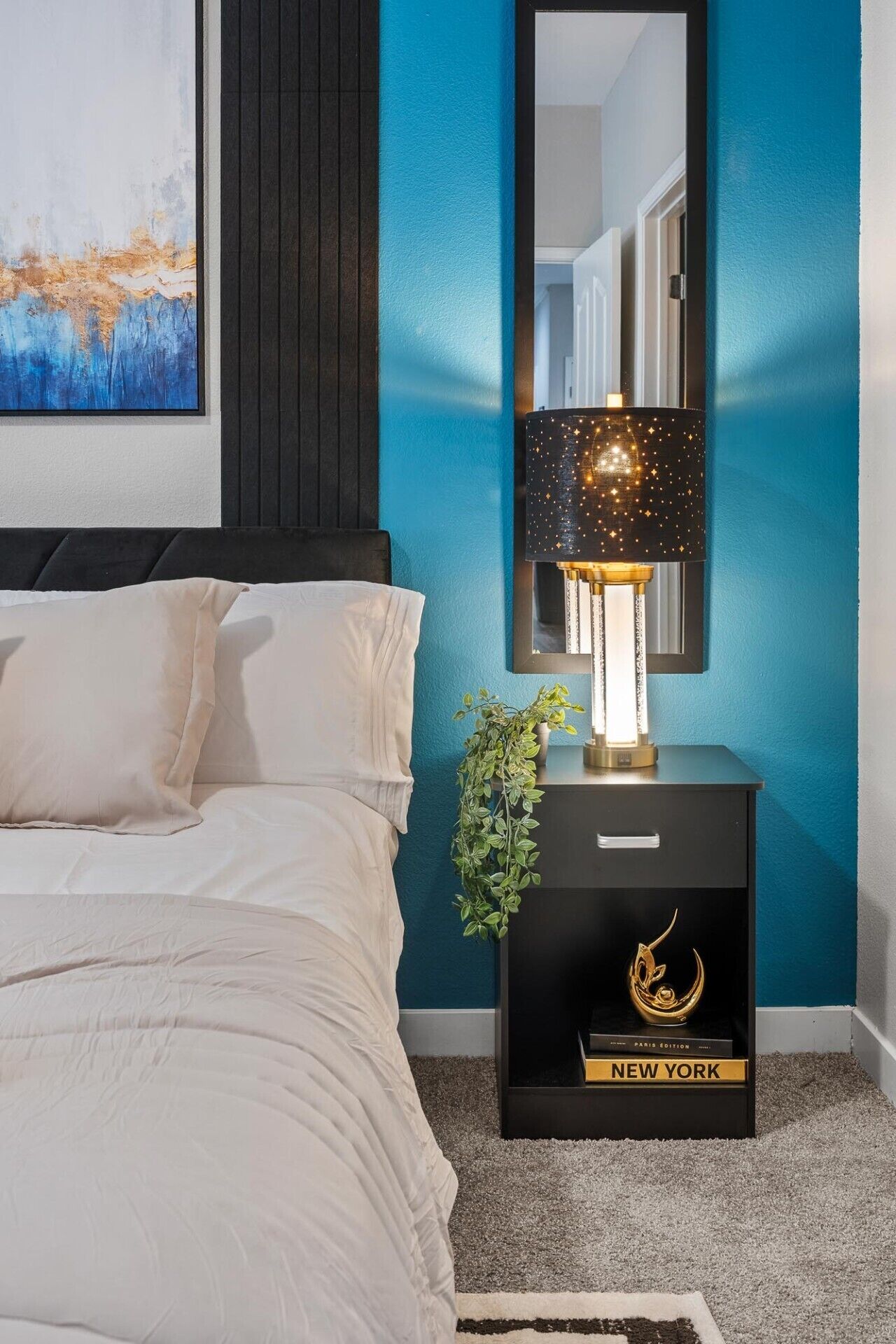 Une chambre à coucher avec un lit, une table de chevet avec une lampe, un miroir et un tableau encadré accroché au mur.