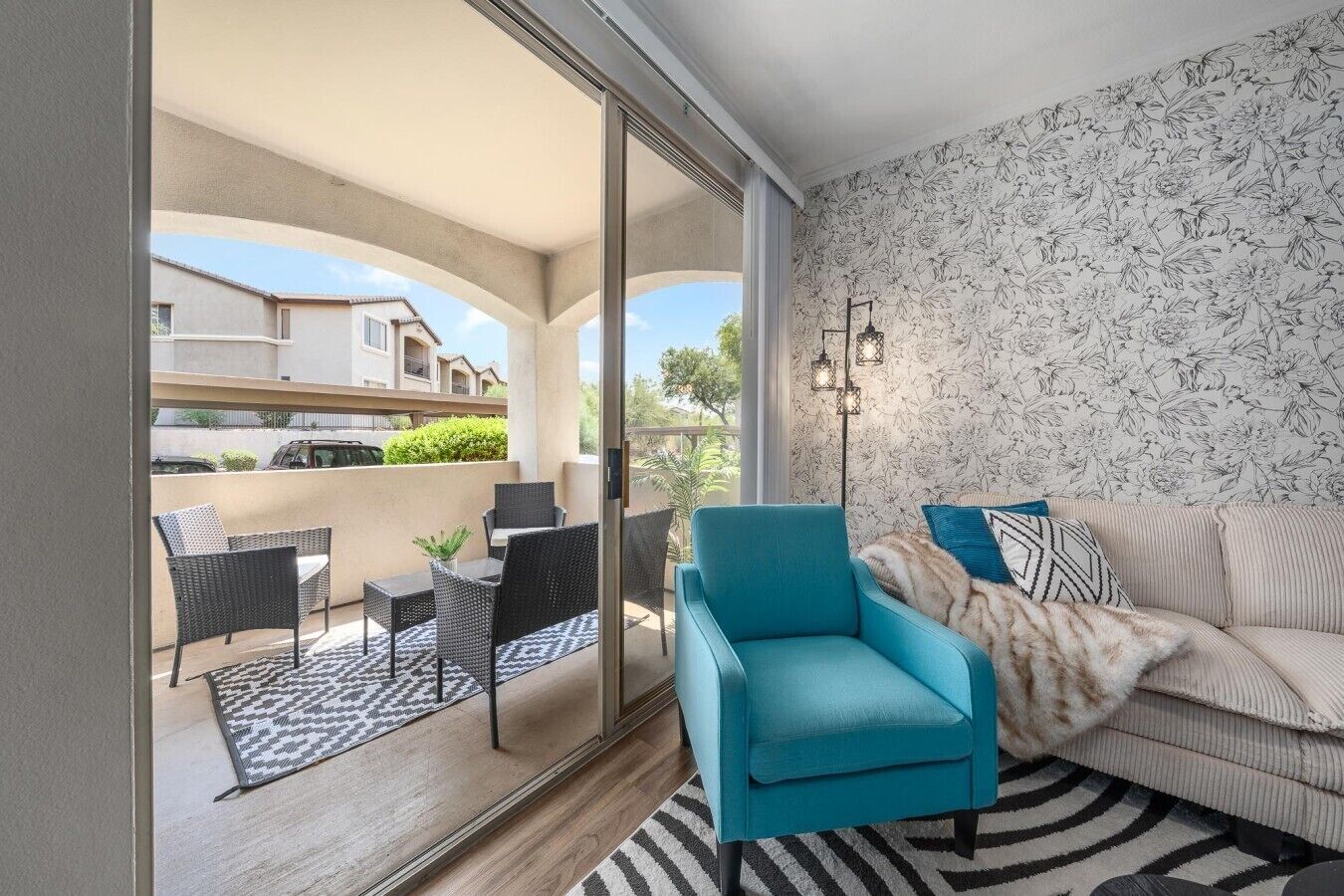 A modern living room with a sofa, a teal armchair, and a dining area with wicker furniture.