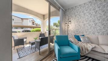 A modern living room with a sofa, a teal armchair, and a dining area with wicker furniture.