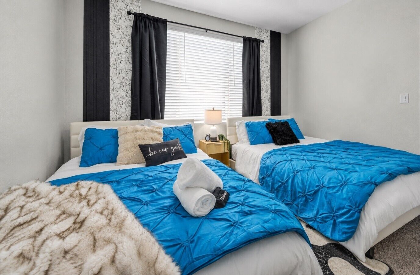 A hotel room with two beds, a nightstand, and a window with curtains.