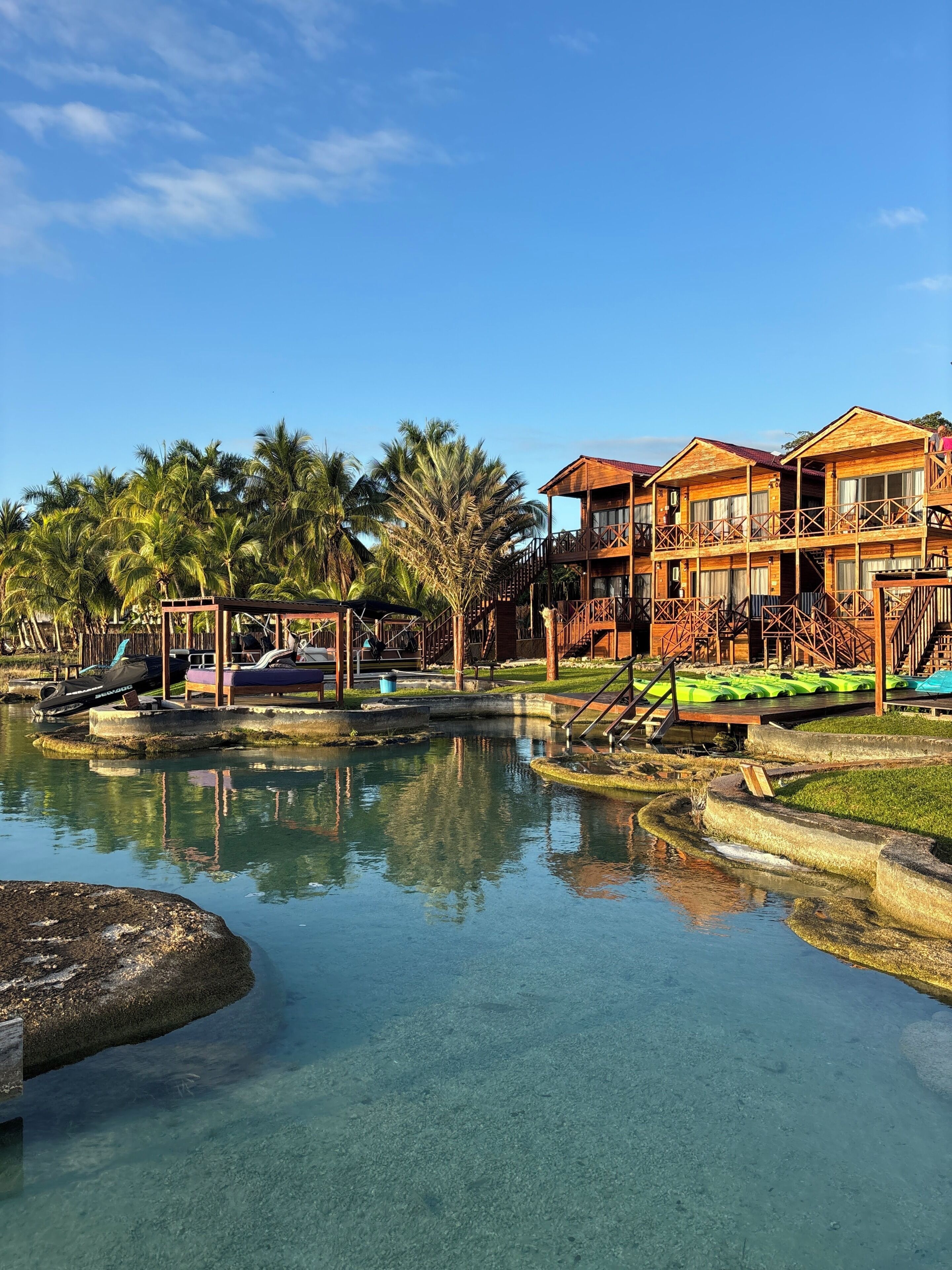 Un resort con edificios de madera, una piscina cristalina y palmeras.